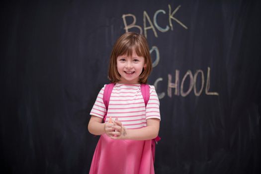 Happy school girl child with backpack writing  back to school on black chalkboard