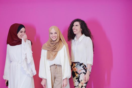 group portrait of beautiful muslim women two of them in fashionable dress with hijab isolated on pink background representing modern islam fashion and ramadan kareem concept