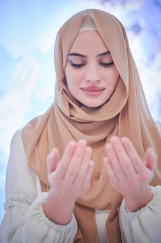 portrait of beautiful muslim woman in fashionable dress with hijab making traditional prayer to God, keeps hands in praying gesture isolated on modern winter mountains background representing modern islam fashion and ramadan kareem concept