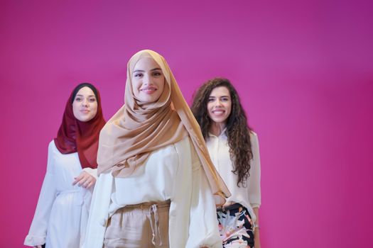 group portrait of beautiful muslim women two of them in fashionable dress with hijab isolated on pink background representing modern islam fashion and ramadan kareem concept