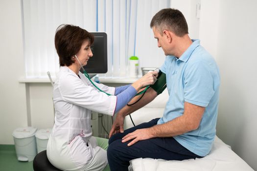 Medical and healthcare concept. Hypertension, high blood pressure and stroke precursors in middle age in men. Medical checkup. Female doctor in general practice measures pressure to patient in clinic.