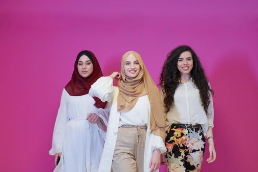 group portrait of beautiful muslim women two of them in fashionable dress with hijab isolated on pink background representing modern islam fashion and ramadan kareem concept