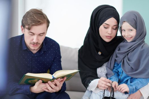 Traditional muslim family parents with children reading Quran and praying together on the sofa before iftar dinner during a ramadan feast at home