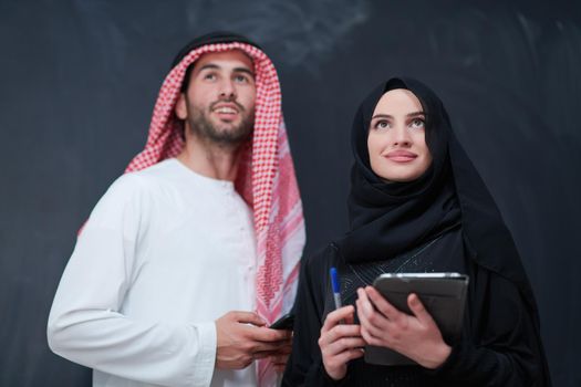 young muslim business couple arabian man with woman in fashionable hijab dress using mobile phone and tablet computer in front of black chalkboard representing modern islam fashion technology and ramadan kareem concept