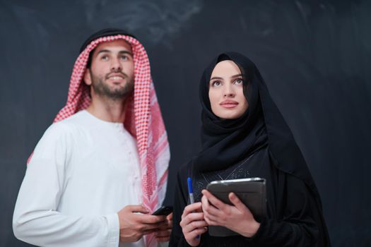 young muslim business couple arabian man with woman in fashionable hijab dress using mobile phone and tablet computer in front of black chalkboard representing modern islam fashion technology and ramadan kareem concept