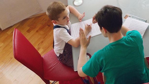 young mom woman doing home work with elementary school grade boy at home in kitchen