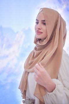 portrait of beautiful muslim woman in fashionable dress with hijab isolated on modern winter mountains background representing modern islam fashion and ramadan kareem concept