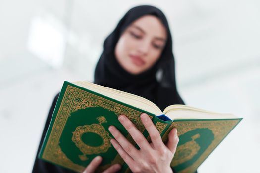 young traditional muslim woman reading Quran on the sofa before iftar dinner during a ramadan feast at home