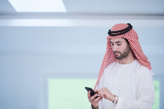 young modern muslim arabian businessman wearing traditional clothes while using smartphone at home