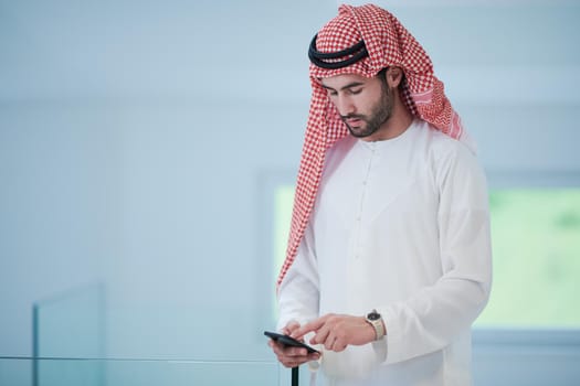 young modern muslim arabian businessman wearing traditional clothes while using smartphone at home