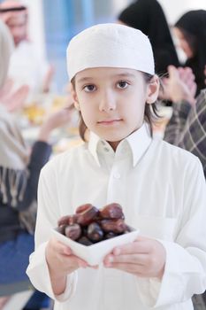Eid Mubarak Muslim family having Iftar dinner little boy holding a plate full of sweet dates to break feast. Eating traditional food during Ramadan feasting month at home. The Islamic Halal Eating and Drinking at modern western Islam