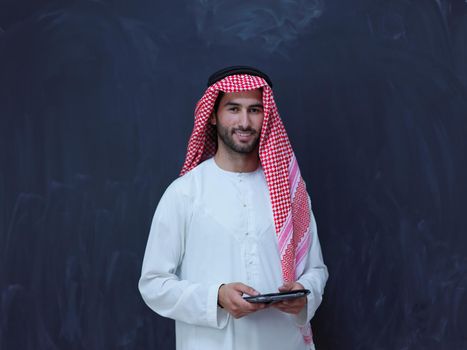 young arabian muslim businessman using tablet computer wearing hijab clothes in front of black chalkboard