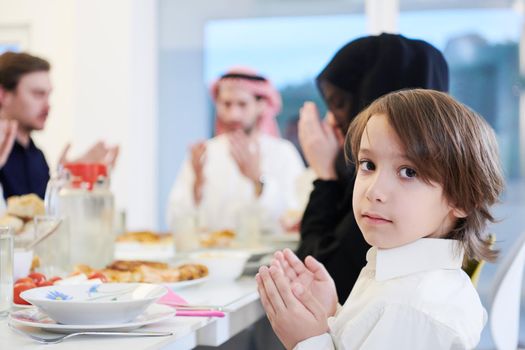little muslim boy praying with traditional family before having iftar dinner together during a ramadan feast at home