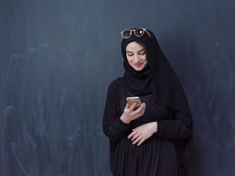 young modern muslim business woman using smartphone wearing sunglasses and hijab clothes in front of black chalkboard