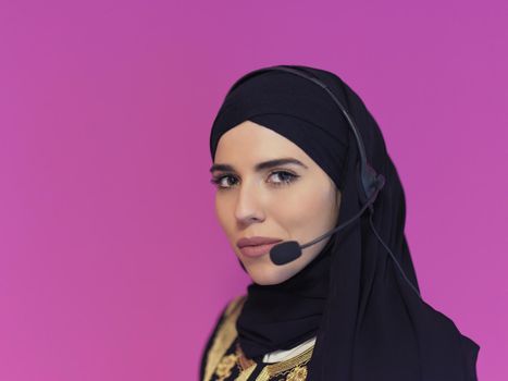 portrait of muslim female with hijab scarf customer representative business woman with phone headset helping and supporting online with customer in modern call centre isolated on pink background