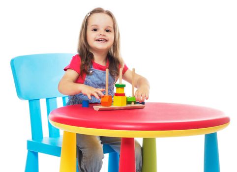 three years old girl sitting at the table and playing, isolated on white