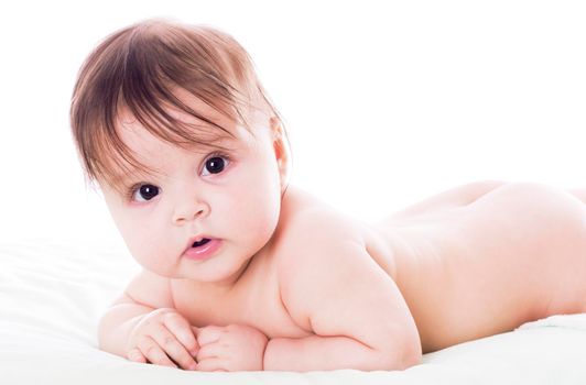 Cute baby lying on stomach on white floor background and smiling big.