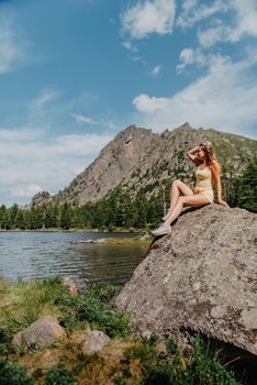 Tourist girl enjoys the magical view of the lake, coniferous forest and magical view sitting on big stone on the shore of a turquoise lake in the mountains. Hiking in the Natural Park. Black lake.