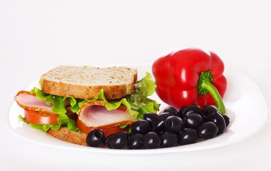 Big healthy sandwich with wholewheat bread, ham, tomatoes,  pepper, olive and curly lettuce on the plate.