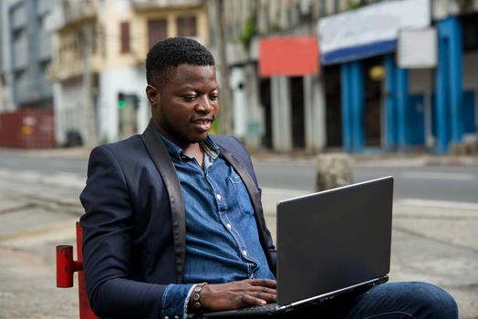 young man sitting in jacket looking at laptop while smiling.