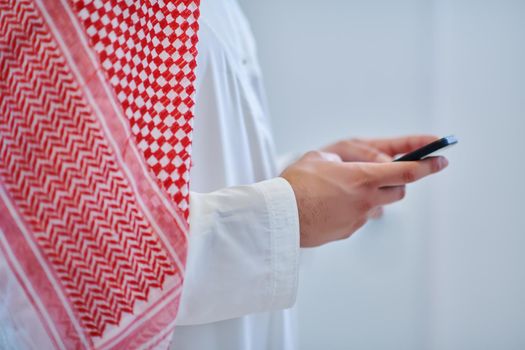 Portrait of young muslim businessman using mobile phone. Successful Arab boy in traditional clothes representing technology