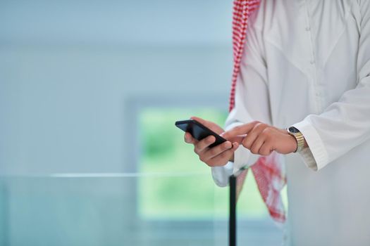 Portrait of young muslim businessman using mobile phone. Successful Arab boy in traditional clothes representing technology