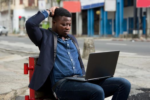 young man in jacket sitting with laptop watching the camera.