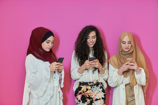 Muslim women using mobile phones isolated on pink background. Young and happy Arabic girls while chatting or searching on the internet, browsing