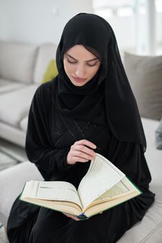 Portrait of young muslim woman reading Quran in modern home. Arabic girl reciting Holy book in islam to worship to Allah during Ramadan.