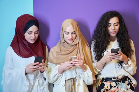 Muslim women using mobile phones isolated on blue and purple background. Young and happy Arabic girls while chatting or searching on the internet, browsing