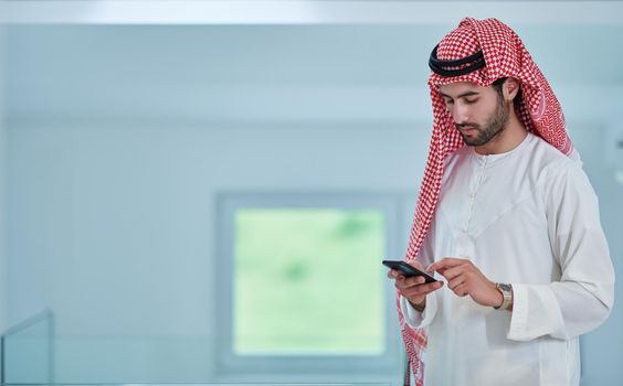 Portrait of young muslim businessman using mobile phone. Successful Arab boy in traditional clothes representing technology