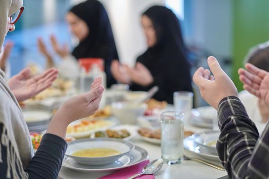 Muslim family making iftar dua to break fasting during Ramadan. Arabian people keeping hands in gesture for praying and thanking to Allah before traditional dinner