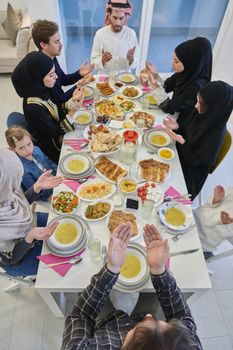 Muslim family making iftar dua to break fasting during Ramadan. Arabian people keeping hands in gesture for praying and thanking to Allah before traditional dinner