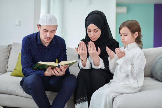 Young muslim family reading Quran during Ramadan. Parents and son worshiping to God, in islamic clothes at modern home