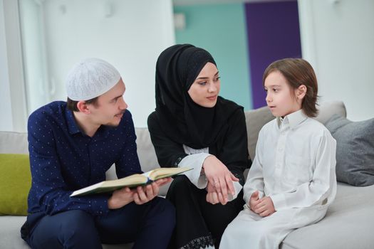 Young muslim family reading Quran during Ramadan. Parents and son worshiping to God, in islamic clothes at modern home