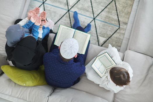 Top view of young muslim family reading Quran during Ramadan. Parents and kids worshiping to God, in islamic clothes at modern home