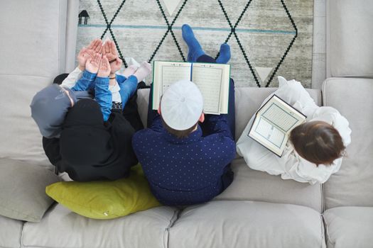 Top view of young muslim family reading Quran during Ramadan. Parents and kids worshiping to God, in islamic clothes at modern home