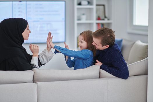 Happy Muslim family spending time together in modern home. Parents playing with daughter on the sofa during Ramadan. Traditional fashionable arabic clothes.