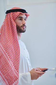 Portrait of young muslim businessman using mobile phone. Successful Arab boy in traditional clothes representing technology