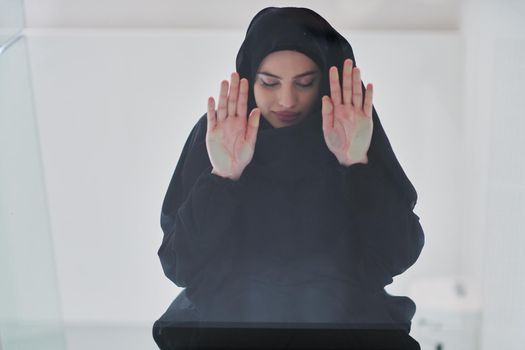 Young muslim woman doing sujud or sajdah on glass floor. Girl wearing black abaya praying salat to God during Ramadan