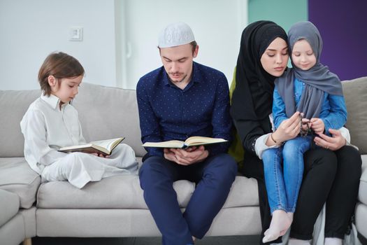 Young muslim family reading Quran during Ramadan. Parents and kids worshiping to God, in islamic clothes at modern home