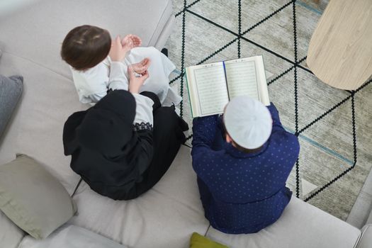 Top view of young muslim family reading Quran during Ramadan. Parents and son worshiping to God, in islamic clothes at modern home