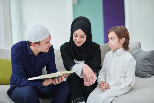 Young muslim family reading Quran during Ramadan. Parents and son worshiping to God, in islamic clothes at modern home