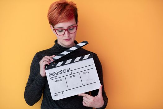 redhead woman holding movie clapper isolated against yellow background  cinema concept in studio
