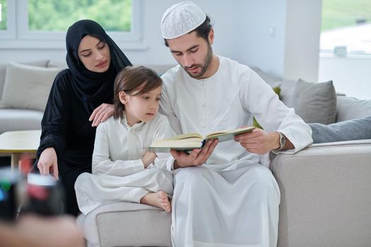 Young muslim family reading Quran during Ramadan. Parents and son worshiping to God, in islamic clothes at modern home