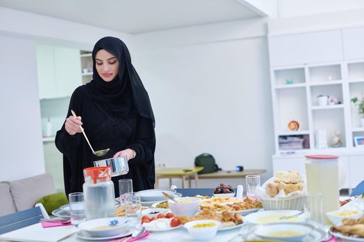 Young muslim woman serving food for iftar during Ramadan. Happy young arabian girl in traditional clothes preparing table for family dinner