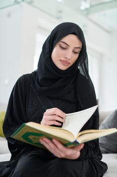 Portrait of young muslim woman reading Quran in modern home. Arabic girl reciting Holy book in islam to worship to Allah during Ramadan.