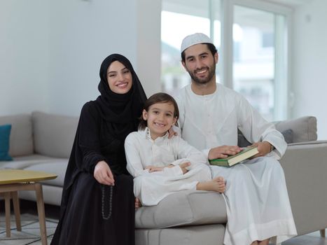 Young muslim family reading Quran during Ramadan. Parents and son worshiping to God, in islamic clothes at modern home