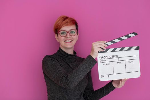 redhead woman holding movie clapper isolated against pink background  cinema concept in studio