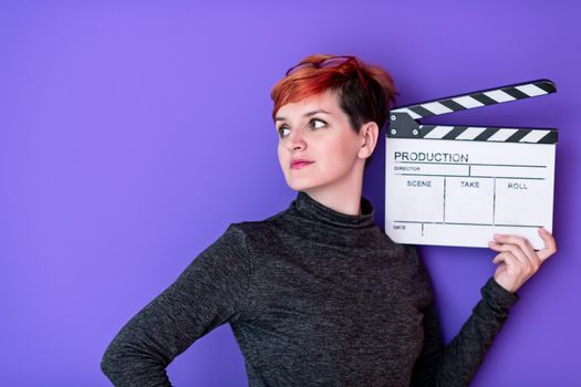 redhead woman holding movie clapper against purple background cinema concept